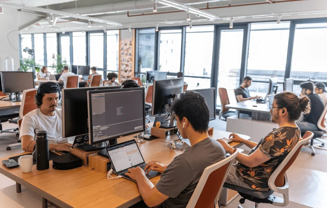 Developers working at their desks in a modern open office, focused on coding and project tasks.