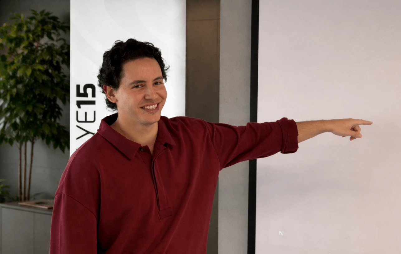 A team member presenting during a Next Talent 2 project demo, confidently pointing at the projected screen in a modern office setting.