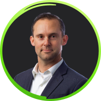 Man with short brown hair wearing a white shirt and dark blazer, smiling against a dark background with a green circular border.