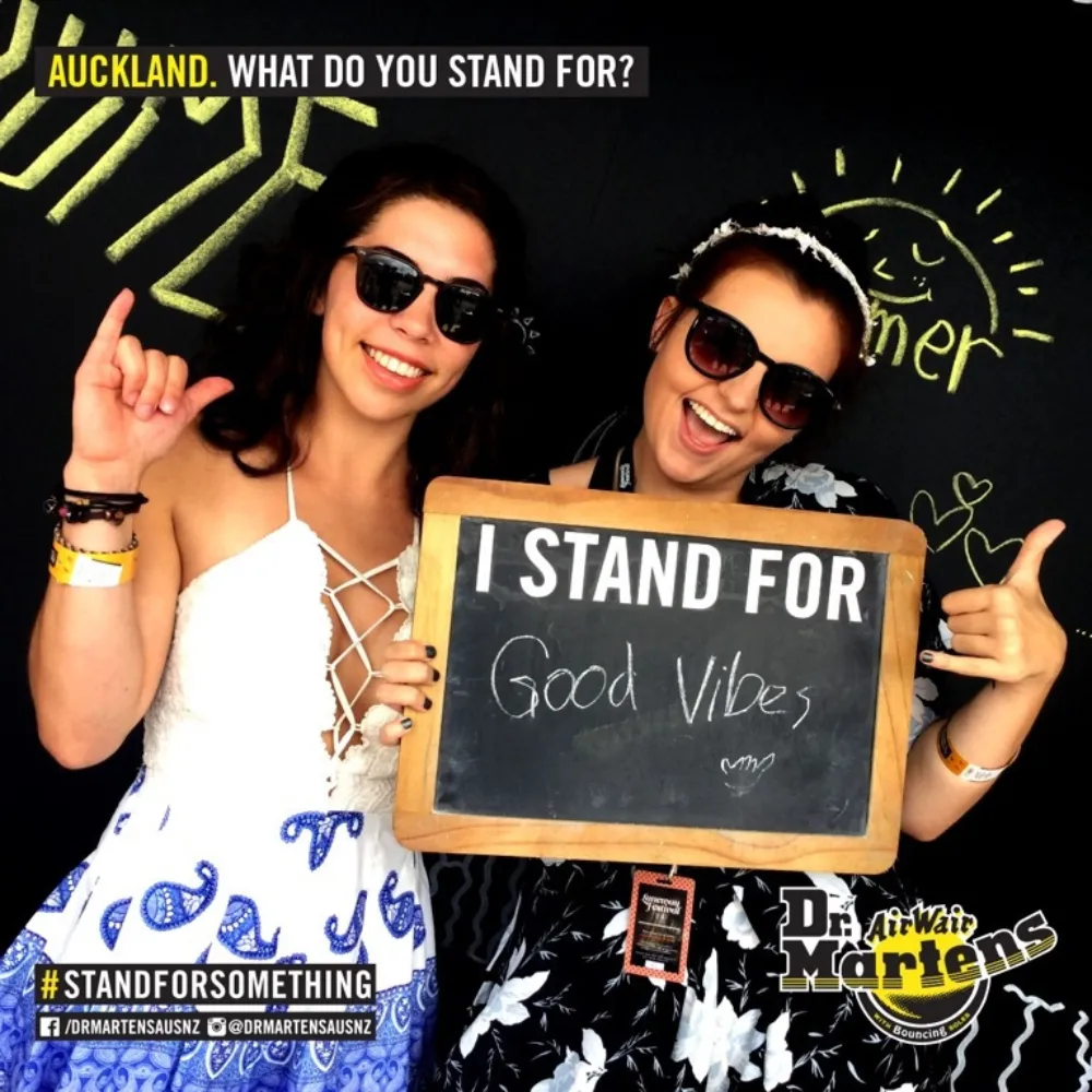 Two women wearing sunglasses holding a chalkboard sign that says I stand for Good Vibes.