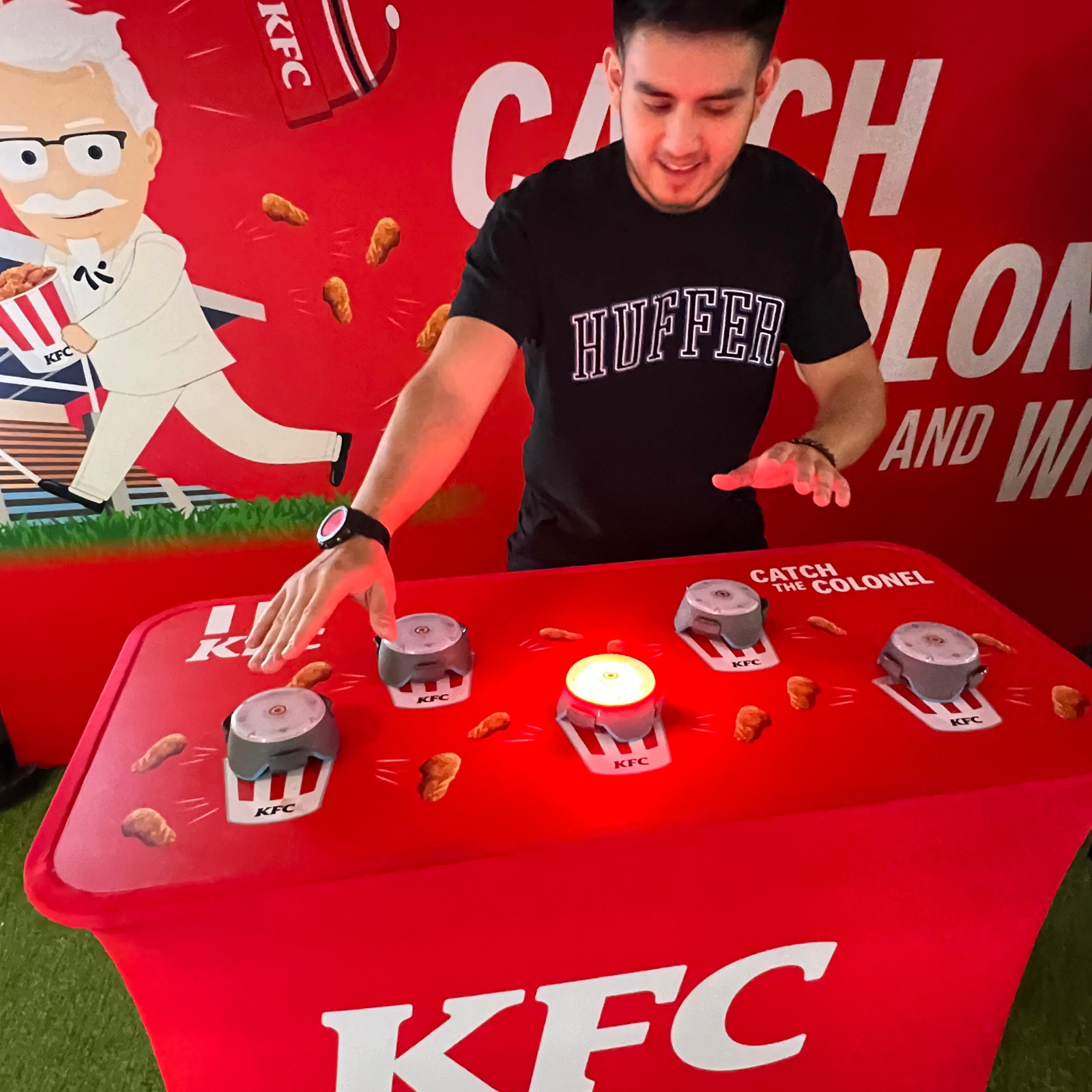 Man playing KFC 'Catch the Colonel' game with lit button on a red game table.