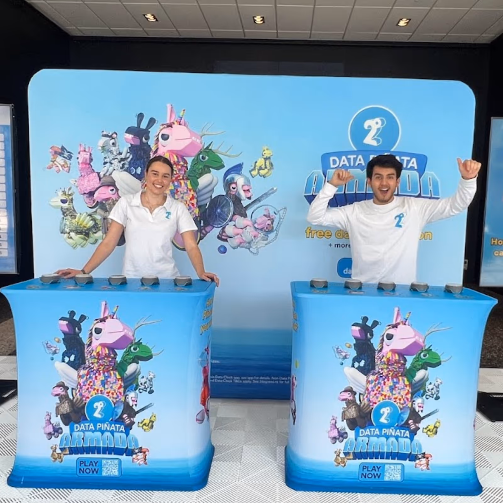 Smiling man and woman at Data Piñata Armada game booths with animated piñata characters on blue backdrop.