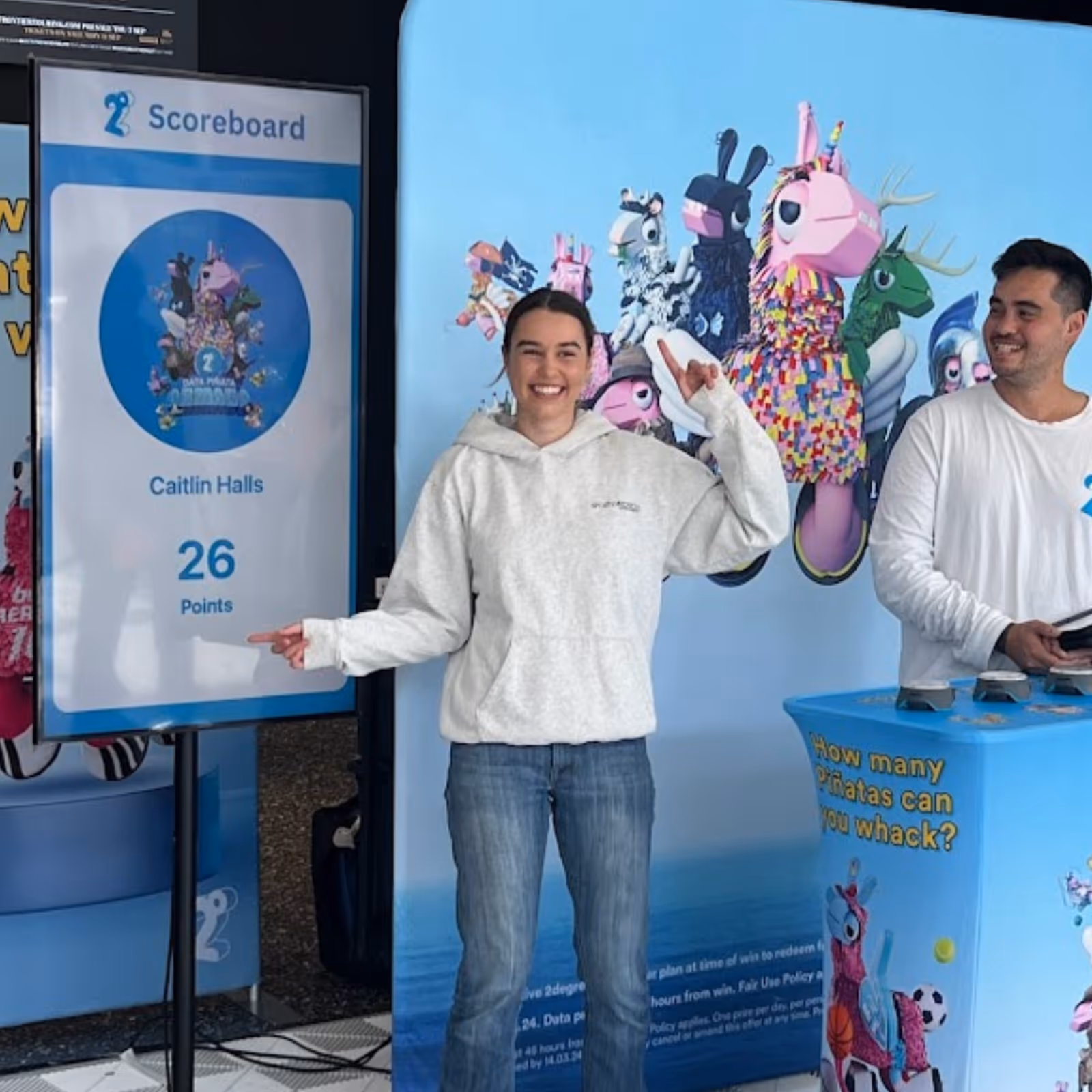 Smiling woman points at scoreboard showing 26 points next to man and colorful piñata characters.