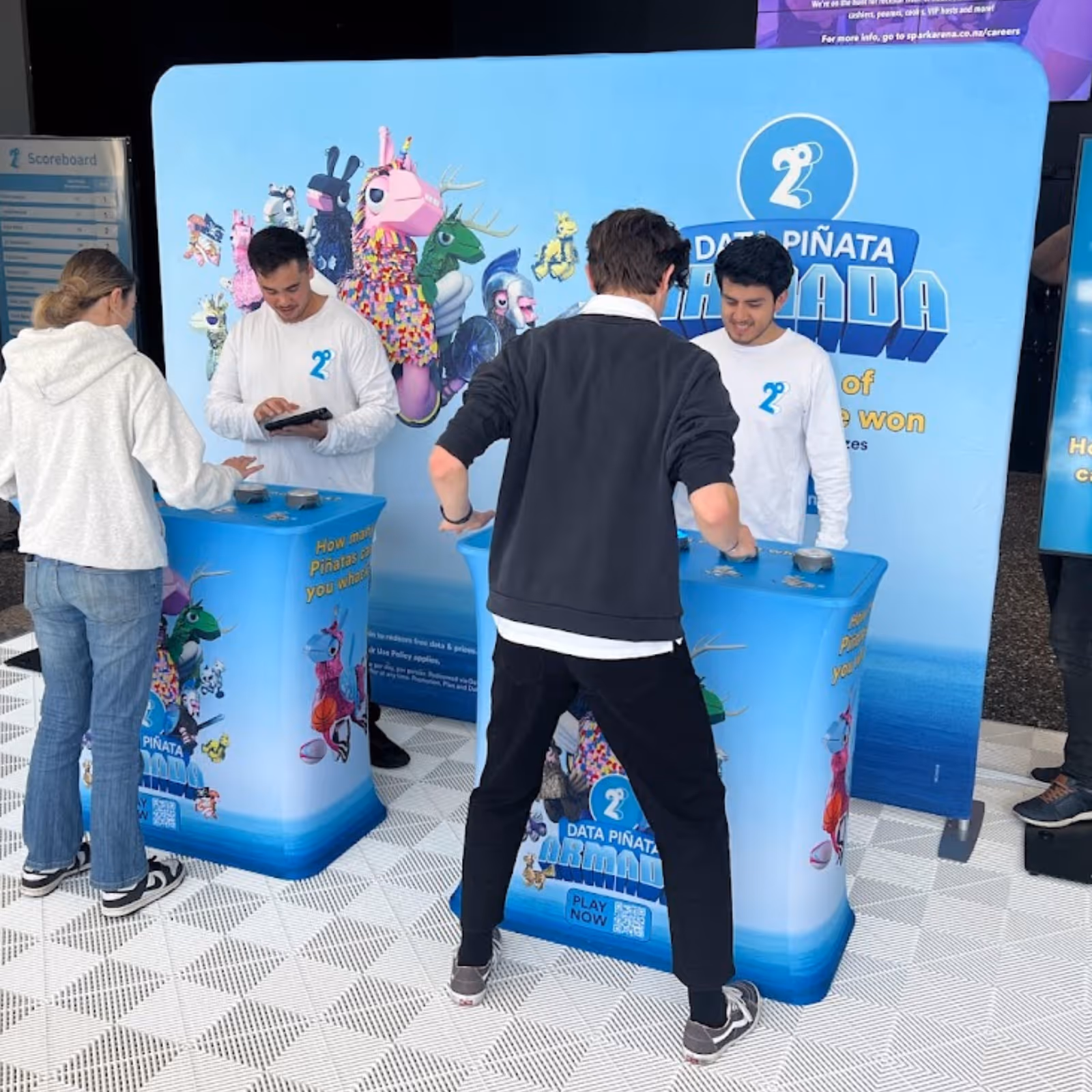 People interacting at a Data Piñata Armada game booth with colorful character graphics and staff in white shirts.