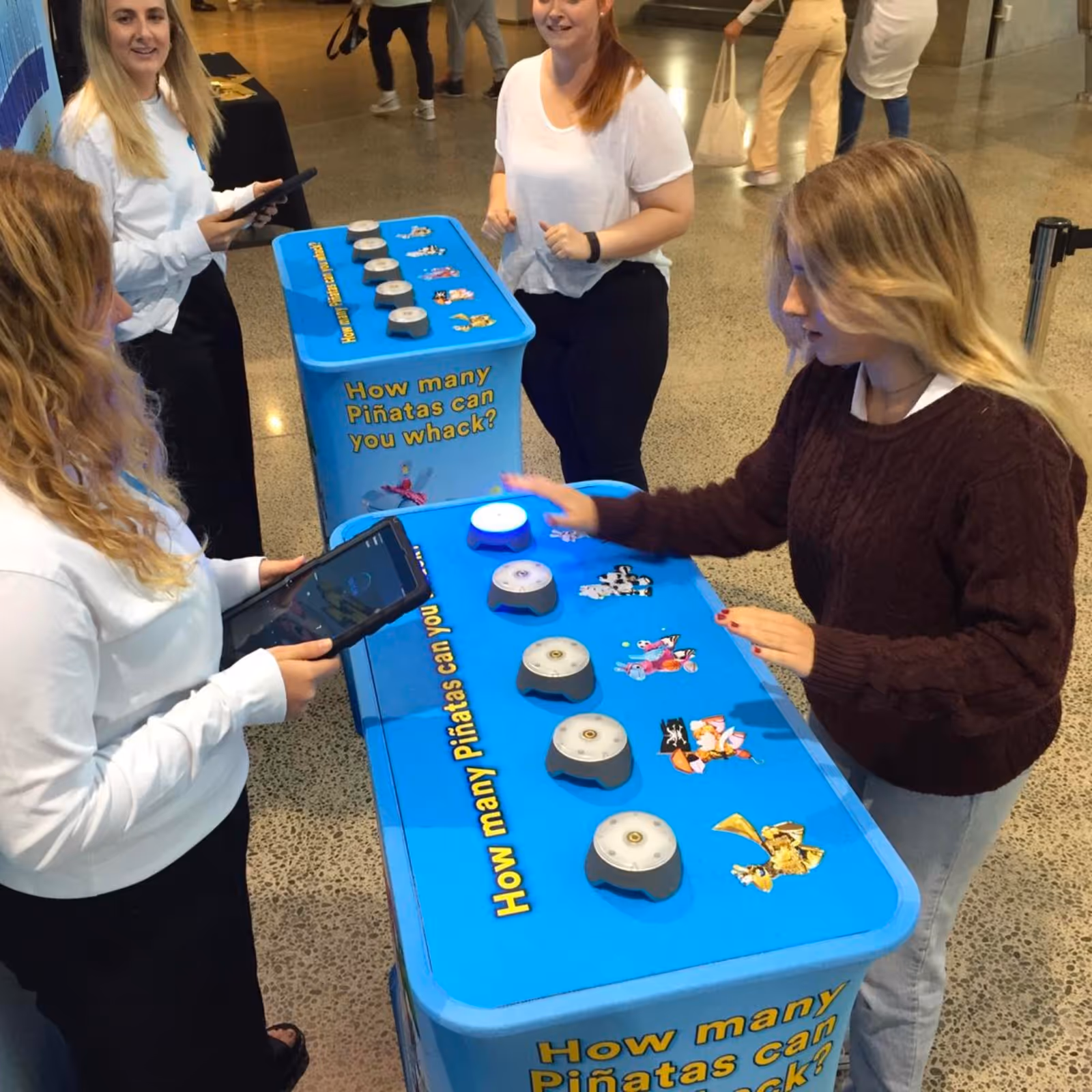 Young woman playing interactive game whacking lights on blue game table labeled 'How many Piñatas can you whack?'