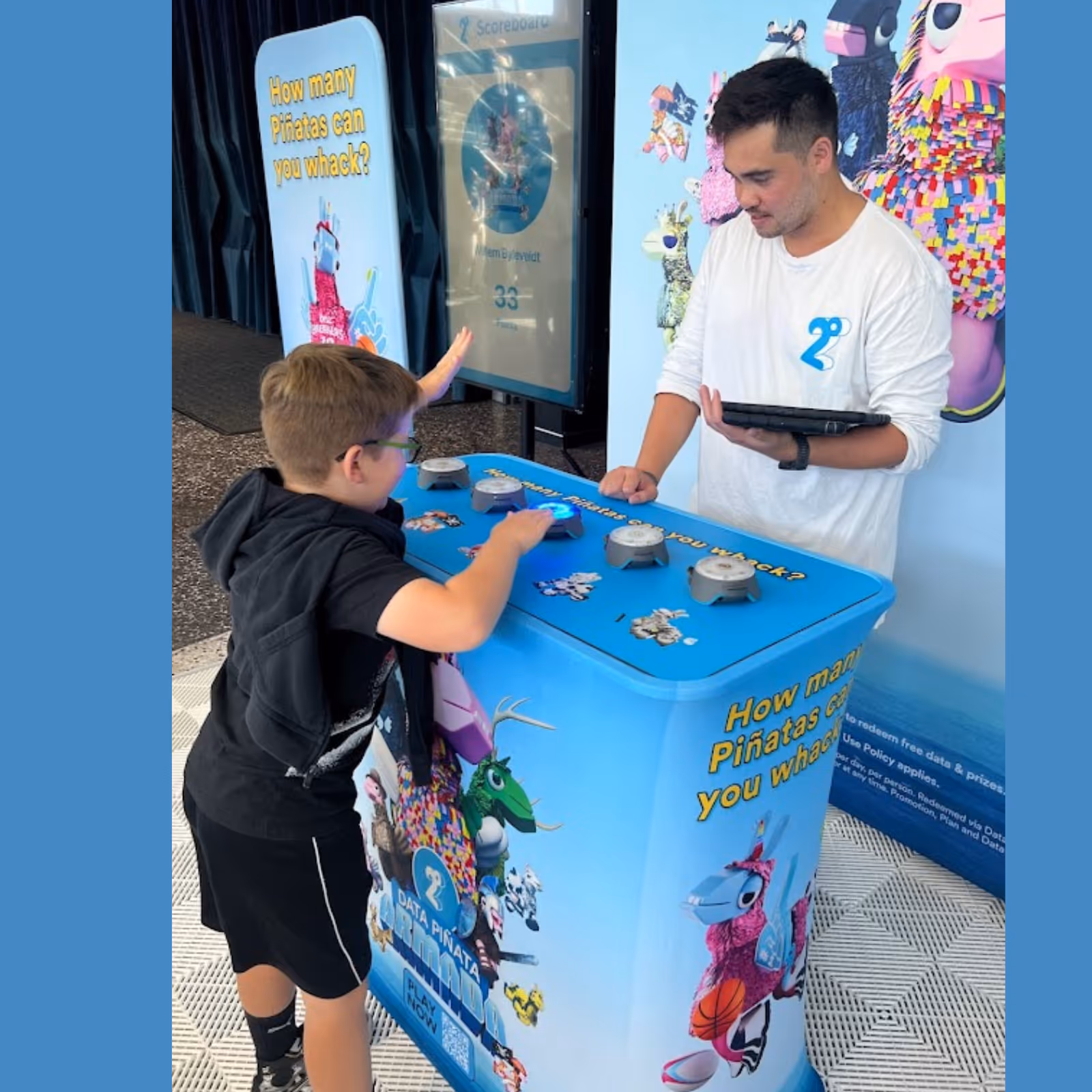 Boy playing a blue interactive piñata whacking game while a man watches holding a tablet.