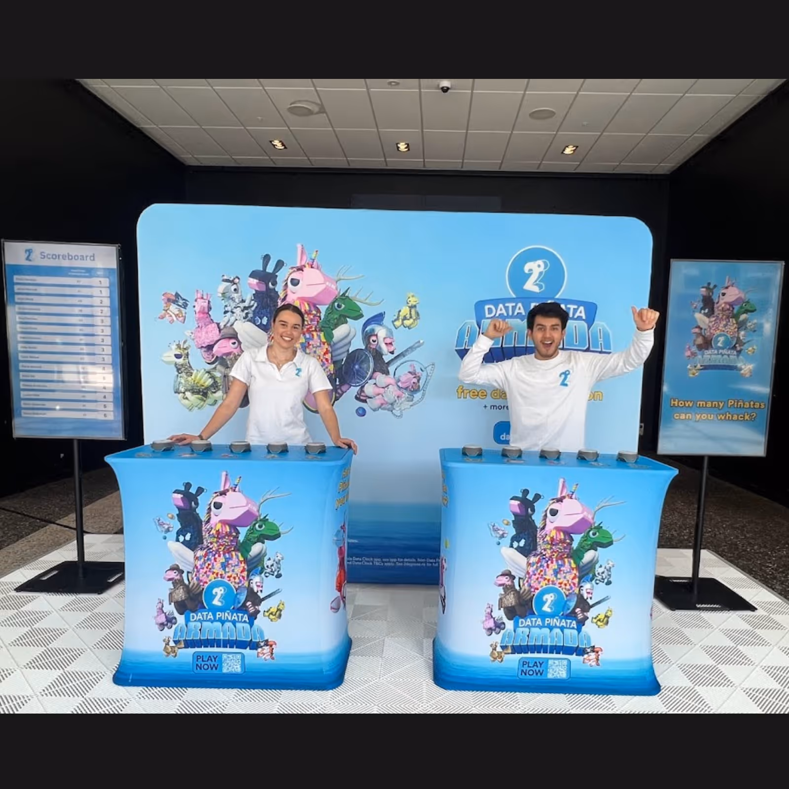 Two people at Data Piñata Armada game booths with colorful piñata characters and scoreboard screens.