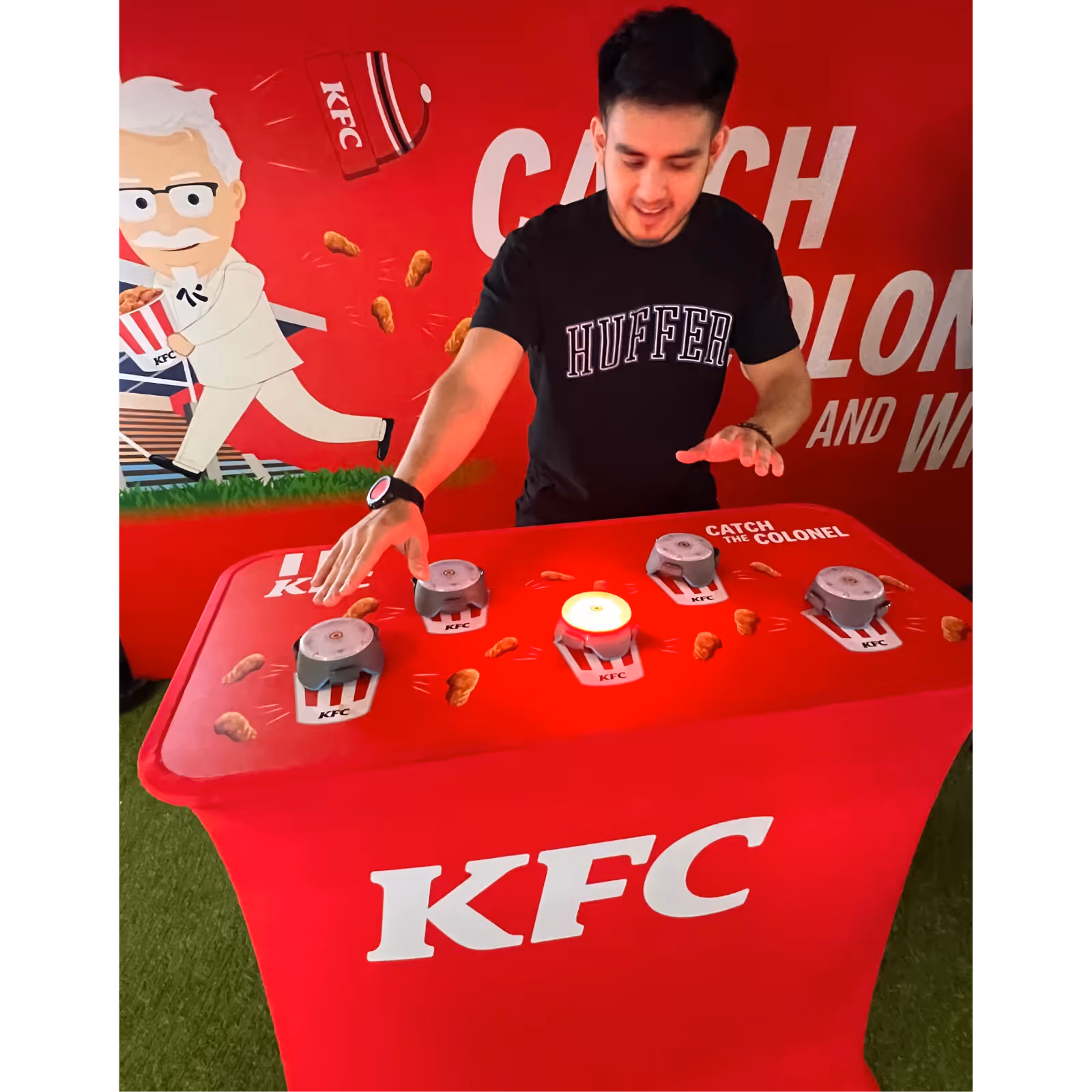 Man playing a KFC Catch the Colonel game pressing a lit button on a red table with KFC branding.