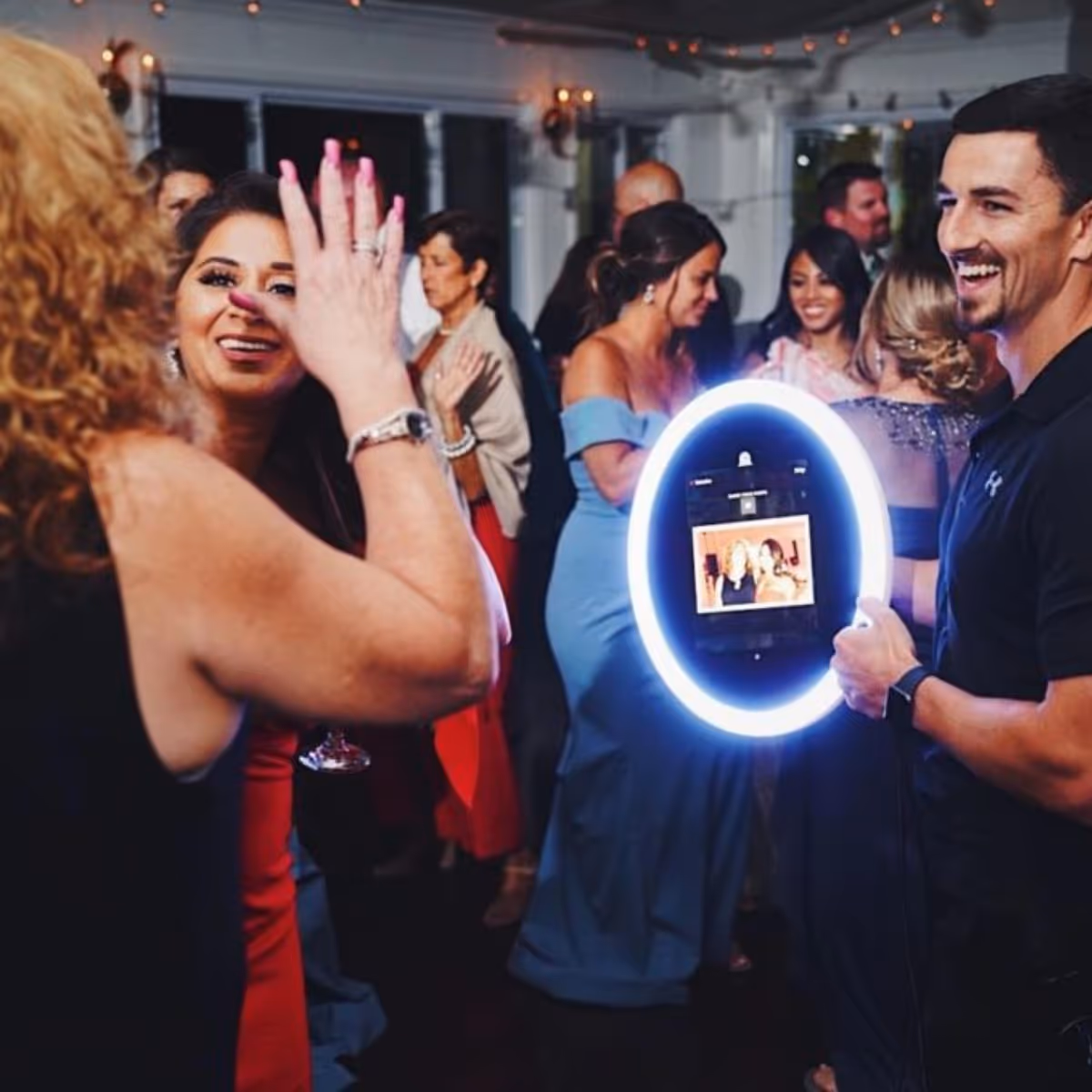 People dressed formally at a party with a man holding a lit ring camera displaying a photo.