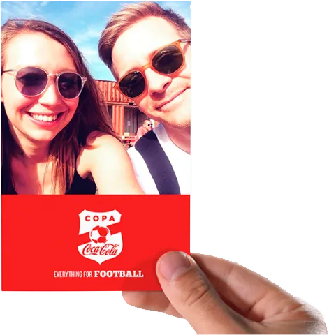 Hand holding a photo of a smiling man and woman wearing sunglasses outdoors in sunny weather.