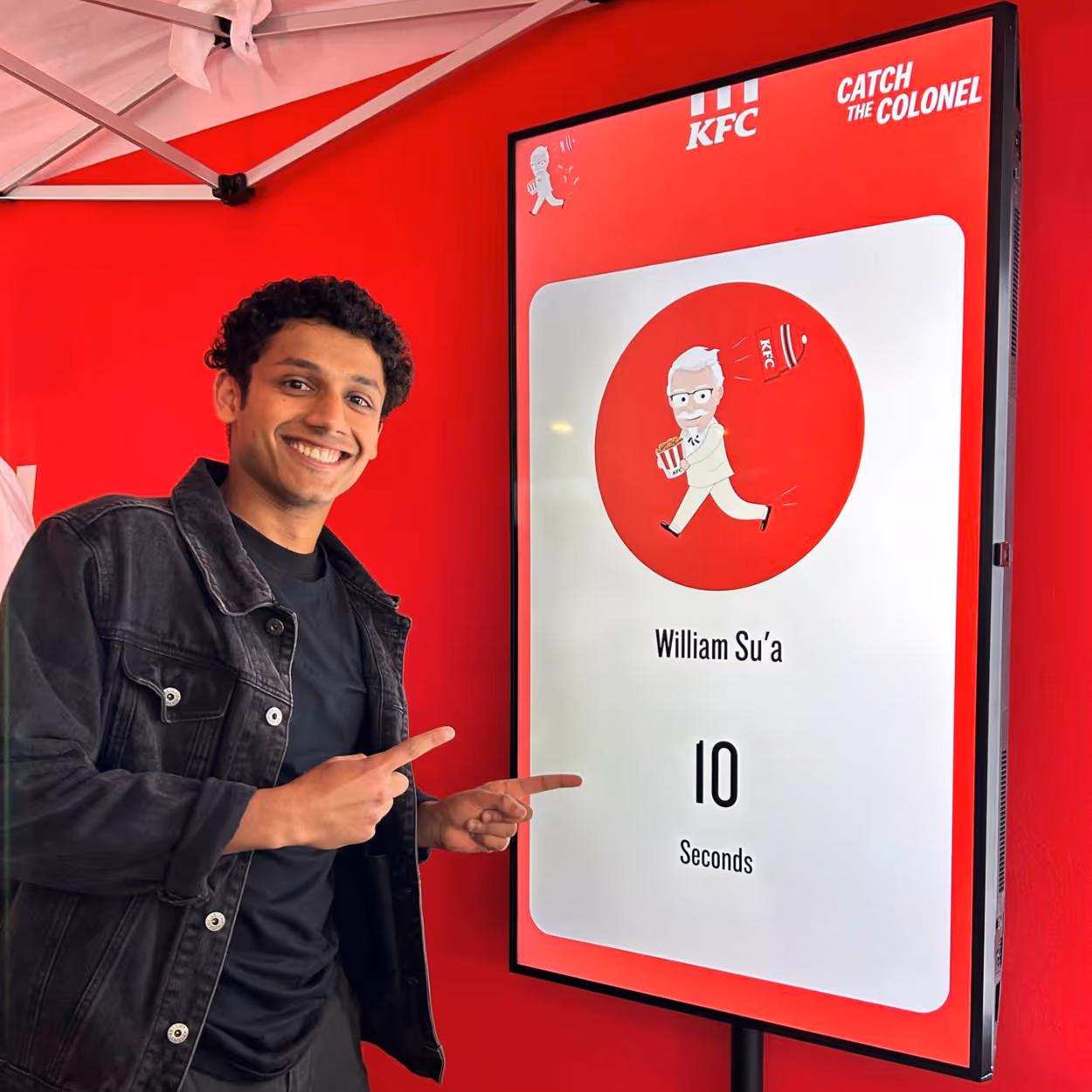 Smiling man pointing at a KFC sign showing score 10 seconds for William Su'a in Catch the Colonel game.