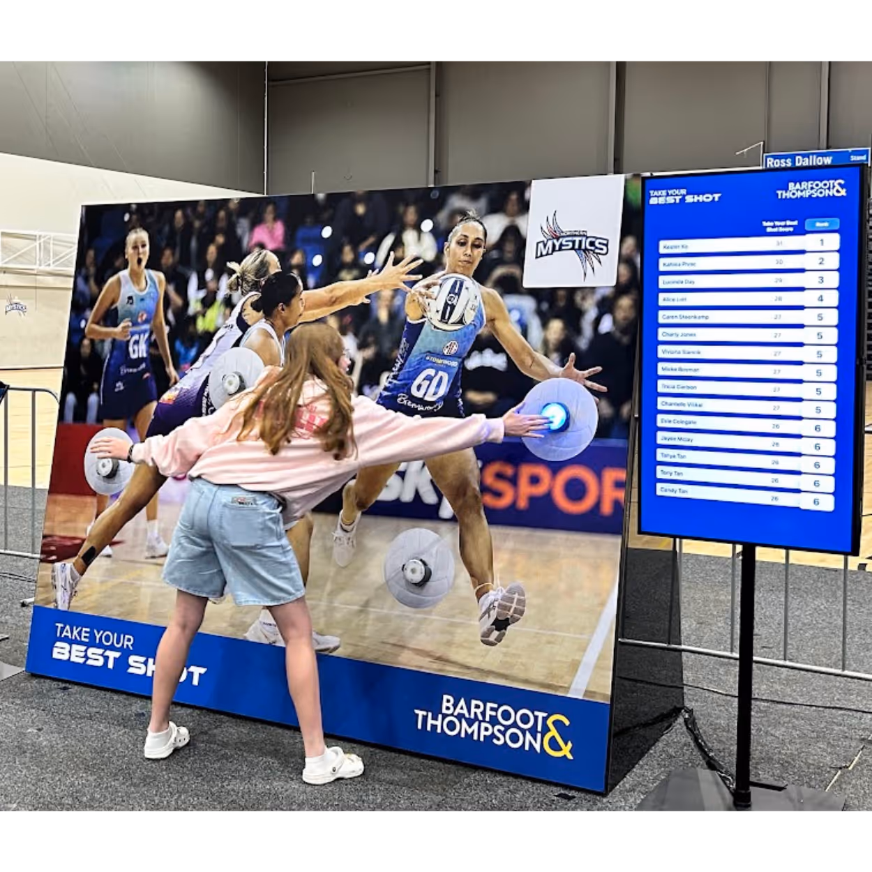 Girl interacts with a netball-themed reaction wall game showing players reaching for a ball with scores on a screen.