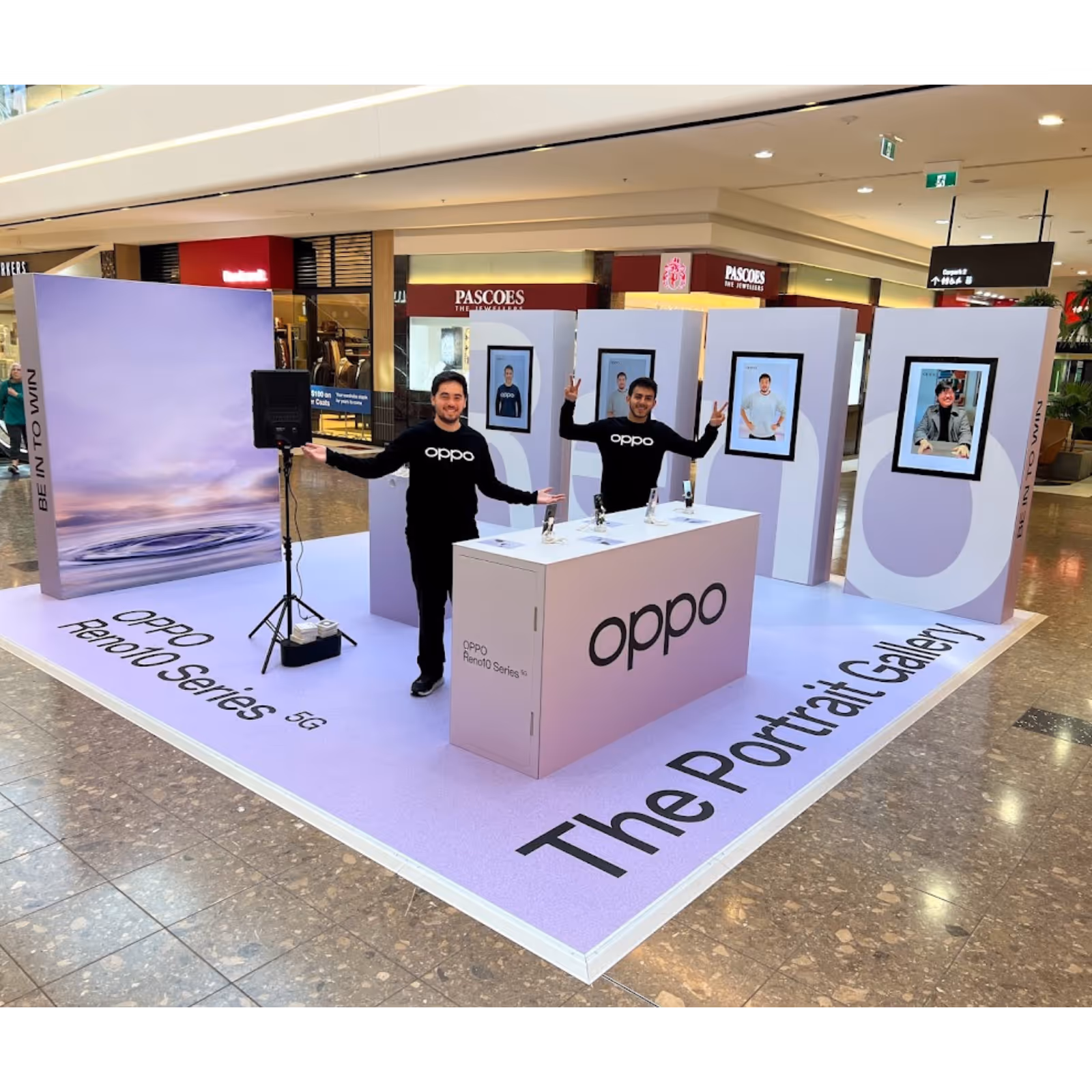 Two men in black Oppo shirts presenting Oppo Reno10 Series 5G phones at a mall portrait gallery display.