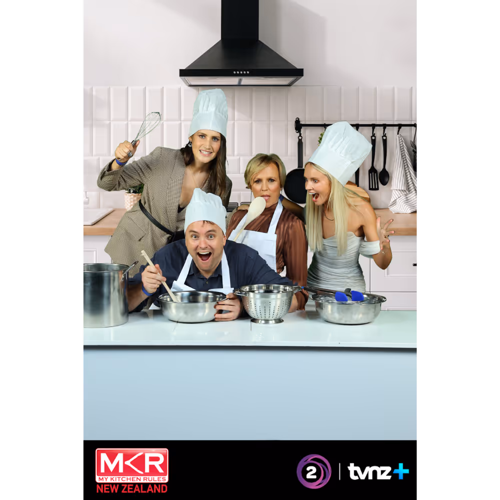 Four people in chef hats and aprons posing in a kitchen with cooking pots and utensils.