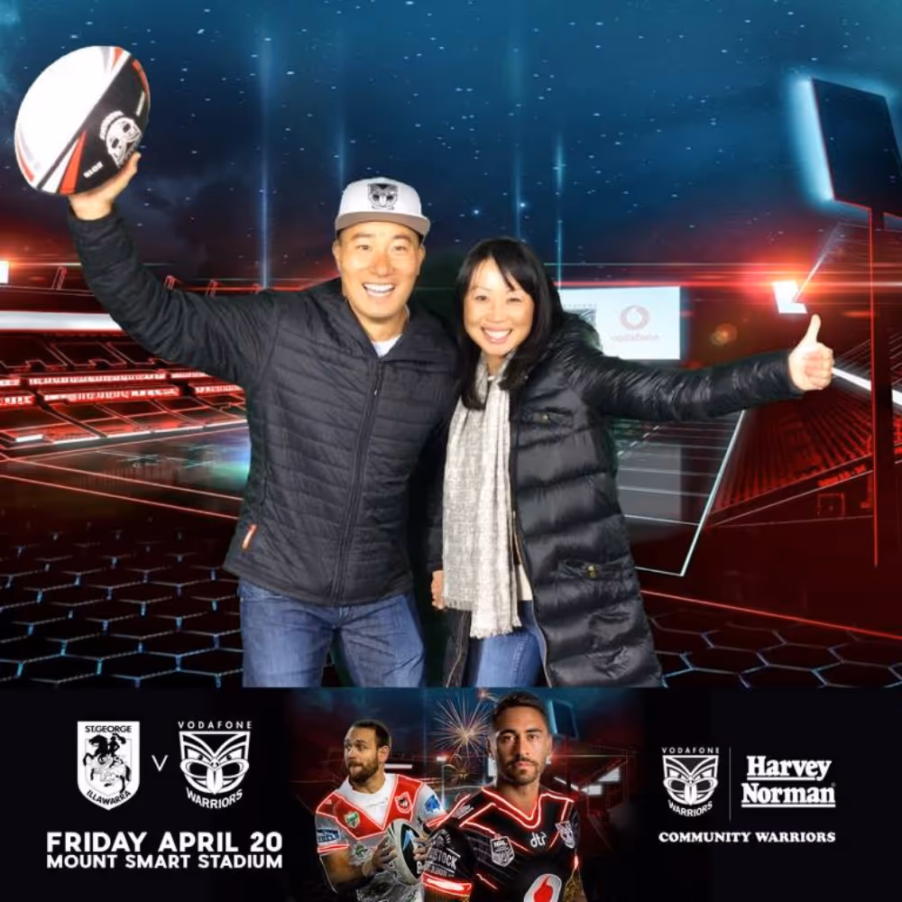 Smiling man and woman in jackets posing with rugby ball and thumbs up in a stadium background.