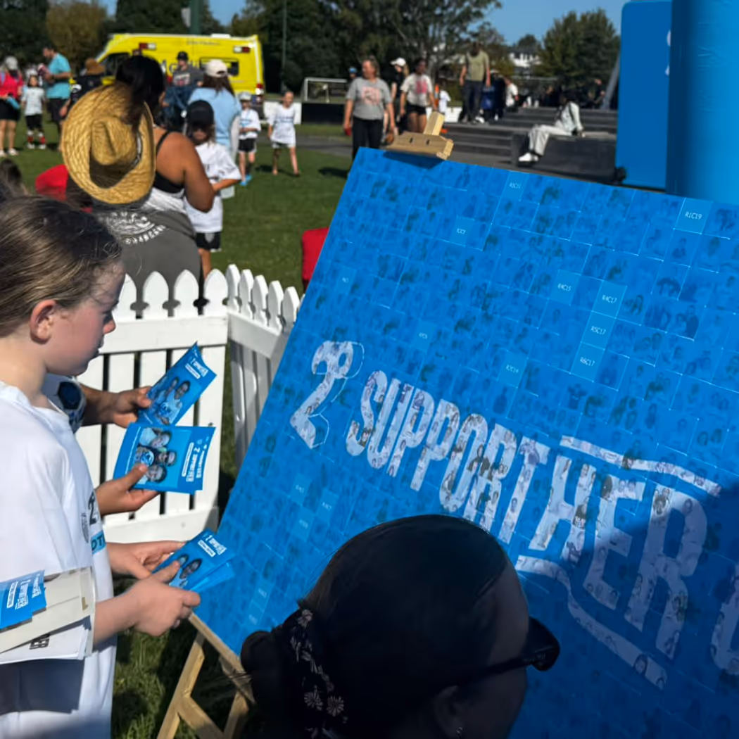 Children holding blue cards while looking at a large board saying '2 Supported' outdoors at an event.