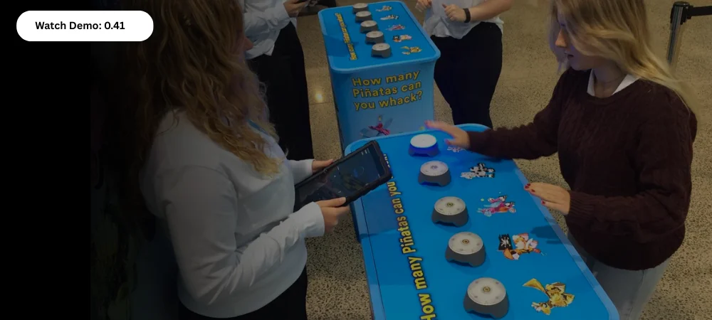 People play a reaction challenge game with multiple whack-a-piñata buttons on a blue table.