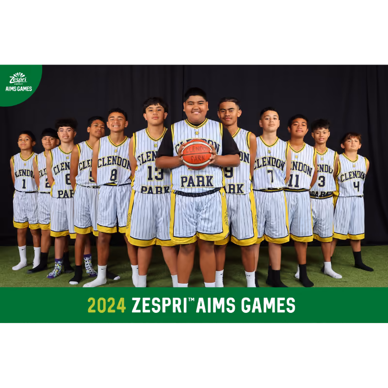 Youth basketball team in Clendon Park uniforms posing in a line with a ball at 2024 Zespri AIMS Games.