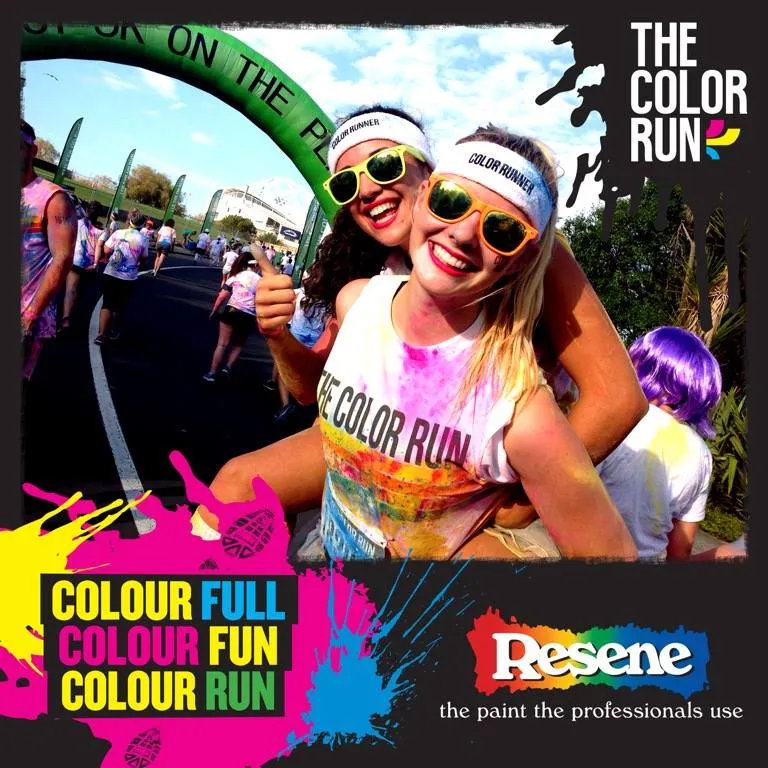 Two smiling women in sunglasses at The Color Run, covered in colorful powder with race crowd behind.