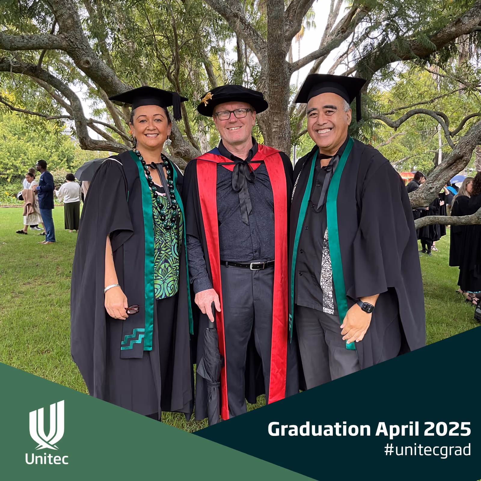 Three smiling graduates in caps and gowns posing outdoors under trees at Unitec April 2025 graduation.