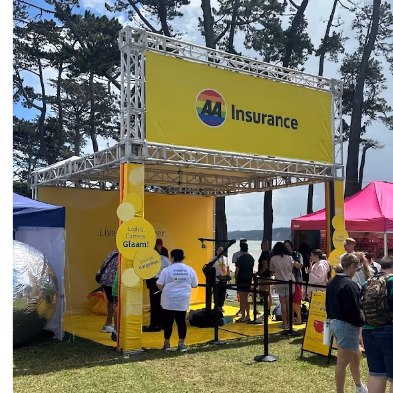 Outdoor AA Insurance booth with yellow banners and people gathered near a lakeside park.