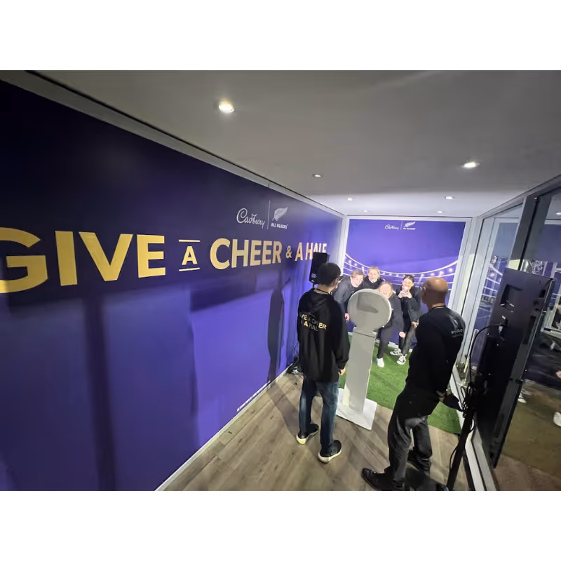 People inside a purple room with wall text 'Give a cheer & a high' taking photos.