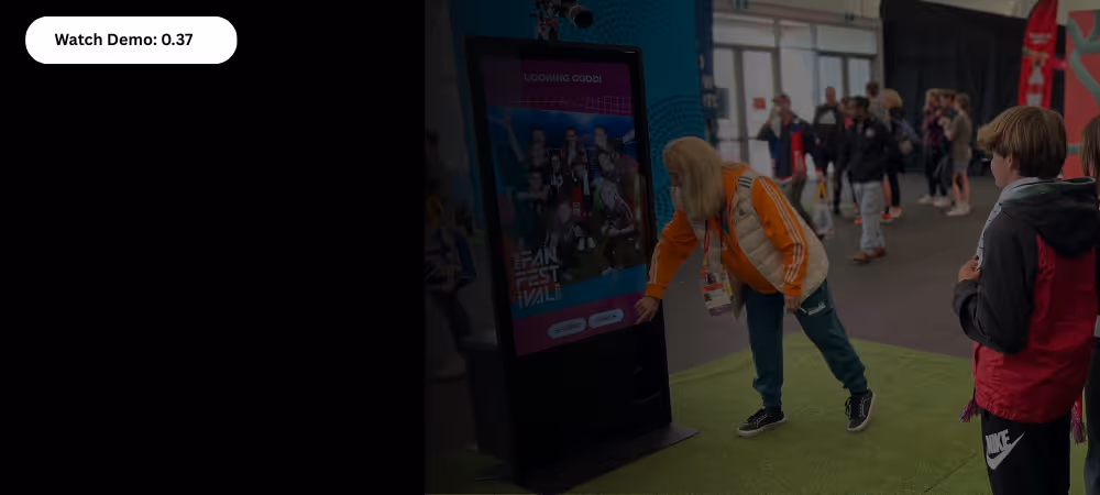 Person interacts with a large touchscreen in a busy indoor space with several onlookers.