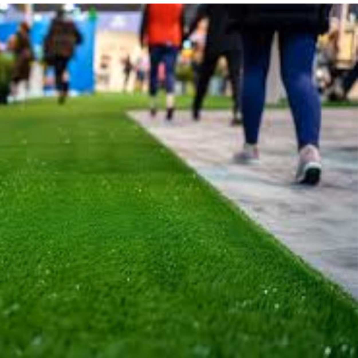 People walking on a paved path beside a green grassy area in an outdoor setting.