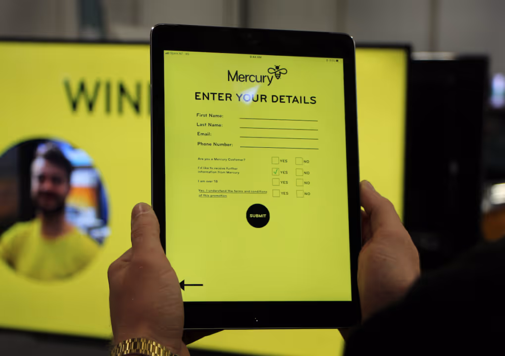 Hands hold a tablet displaying Mercury form asking for name, email, phone, and consent with submit button.
