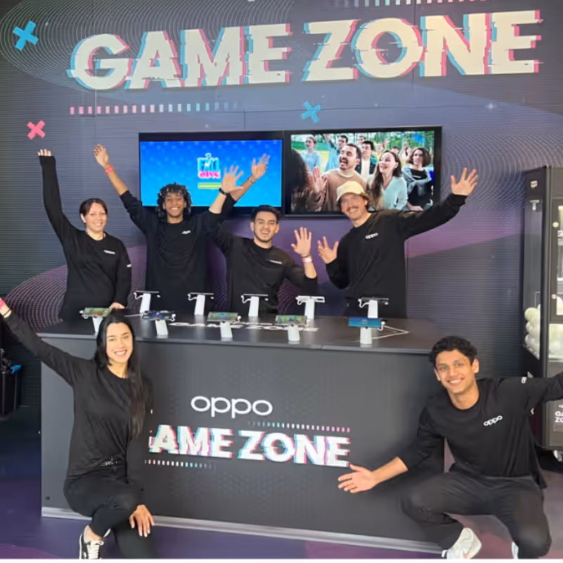 Six people in black shirts posing with raised hands behind a counter labeled OPPO Game Zone.