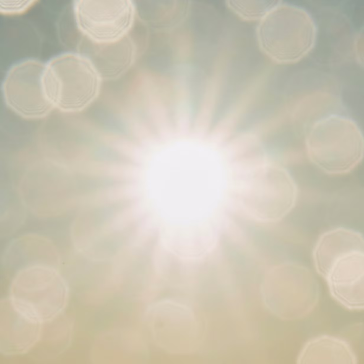Bright sun with radiating light beams and soft lens flares in a hazy sky. The image is slightly overexposed, creating a glowing and ethereal effect.