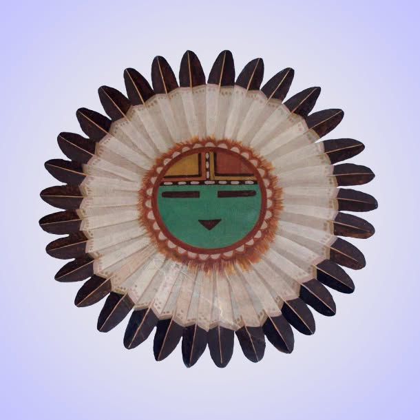 A circular feathered ornament with alternating dark and pale feathers surrounds a central geometric face-like design in green, red, black, and white.