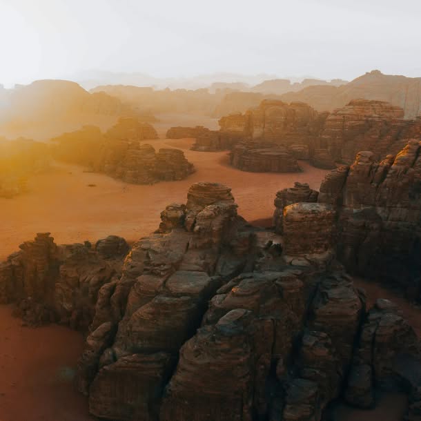 A hazy desert landscape of layered sandstone rock formations and sandy valleys glowing in warm orange light.