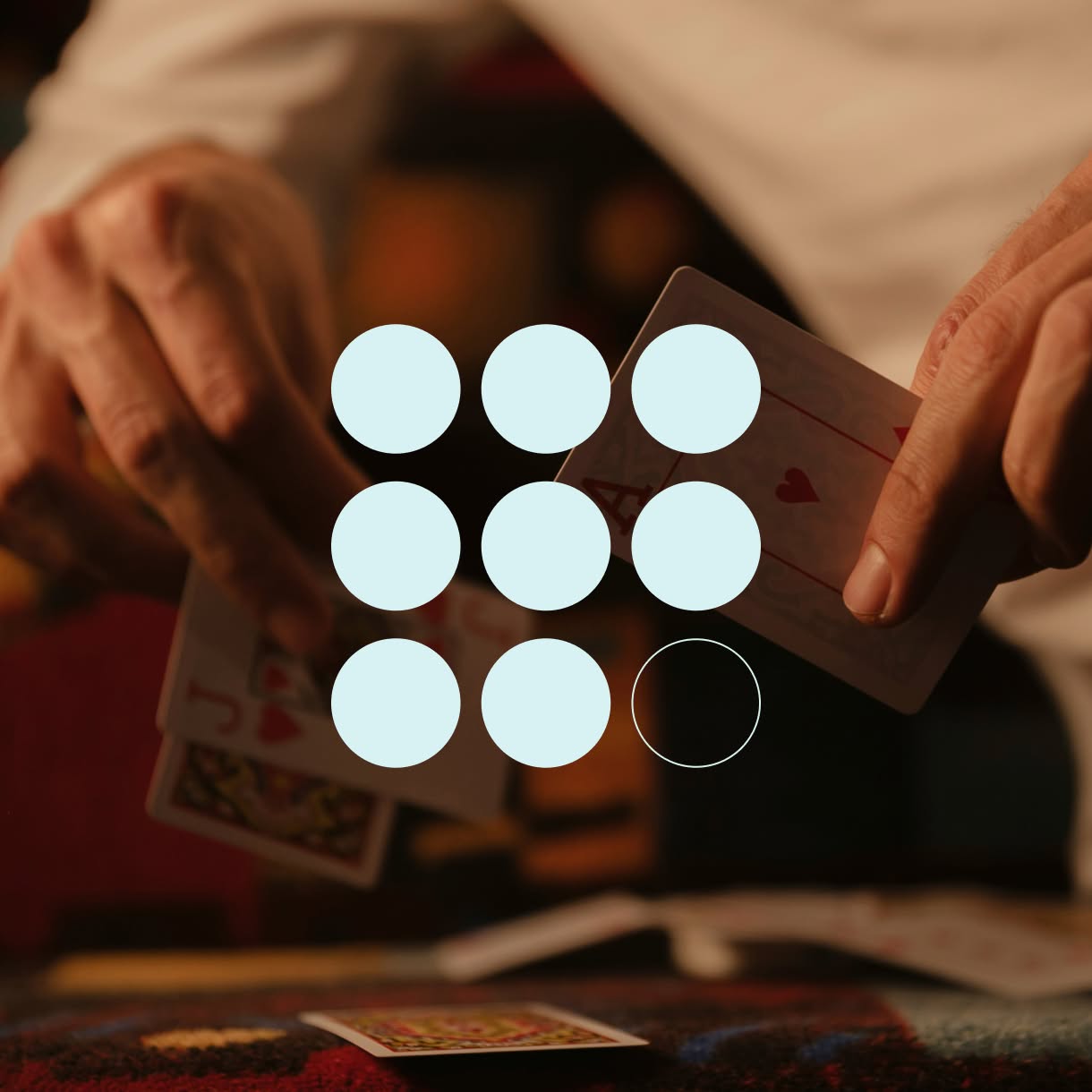 Close-up of hands dealing playing cards, overlaid with a three-by-three grid of pale circles, one shown only as an outline.