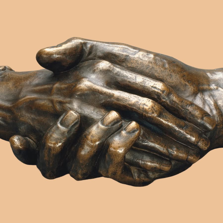 Close-up of a bronze sculpture depicting several hands clasped together in a layered embrace, set against a pale peach background.