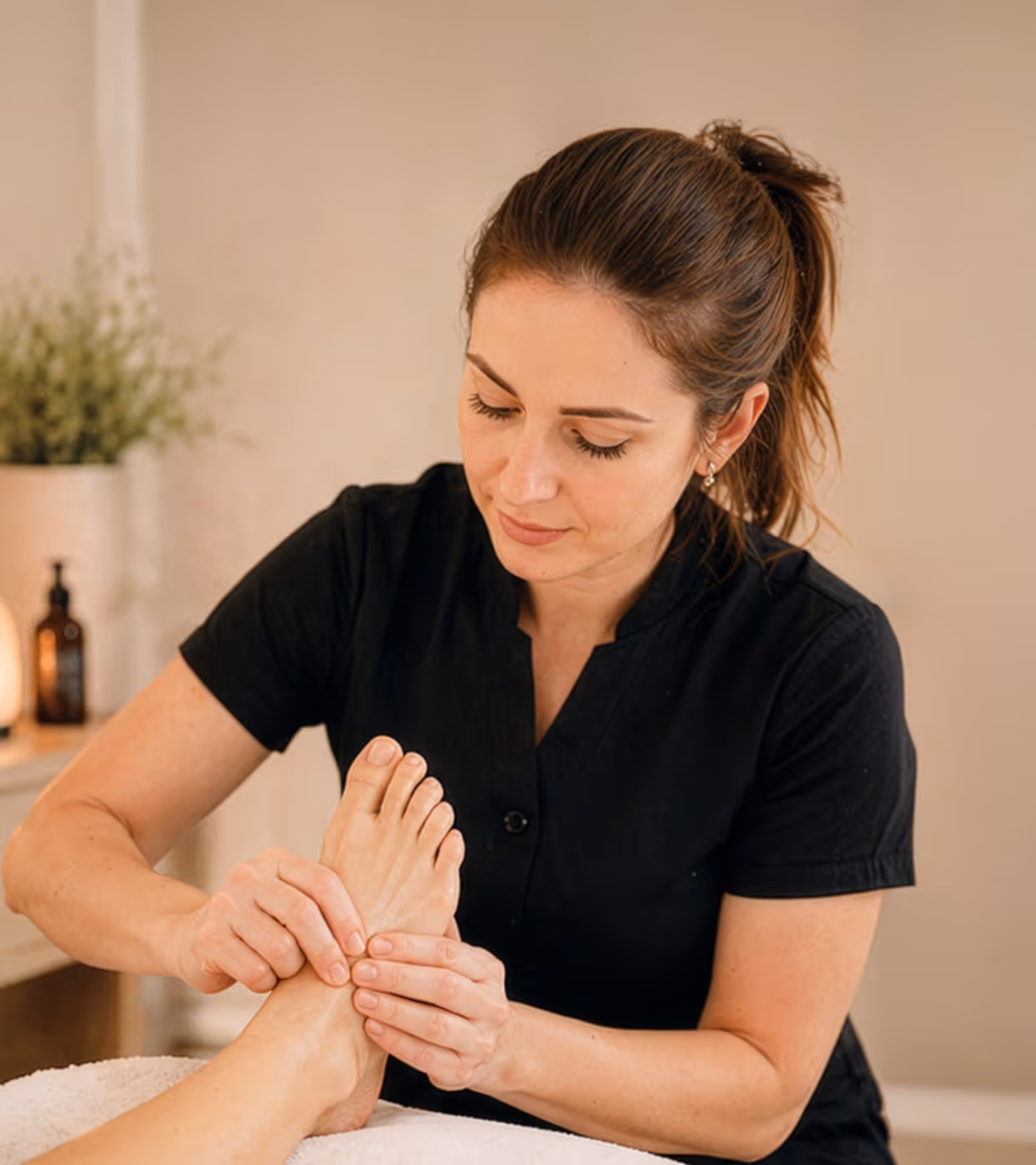 Woman in black shirt giving a foot massage in a calm, softly lit room.
