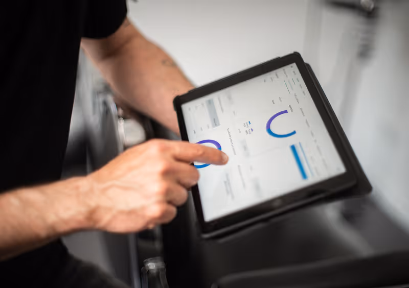 Person pointing at data charts displayed on a tablet screen while standing near exercise equipment.