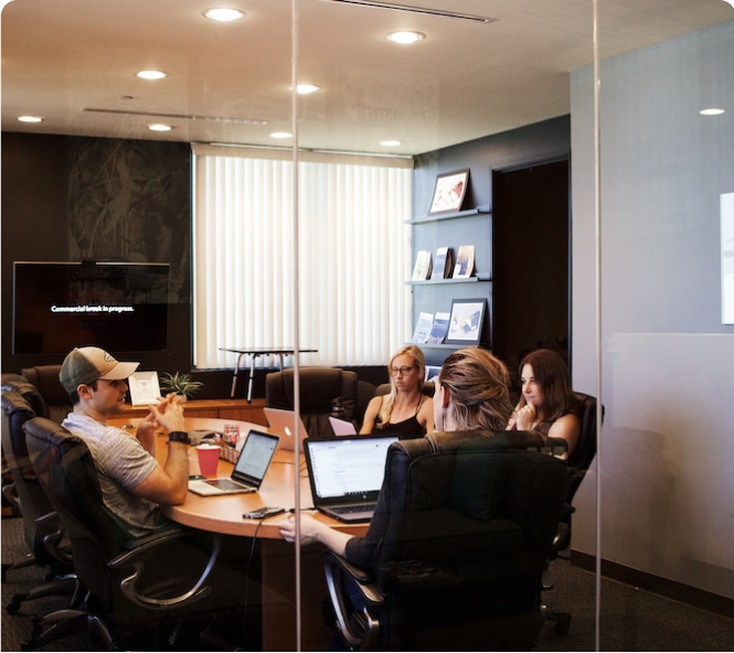several people with laptops sitting around a table in a conference room