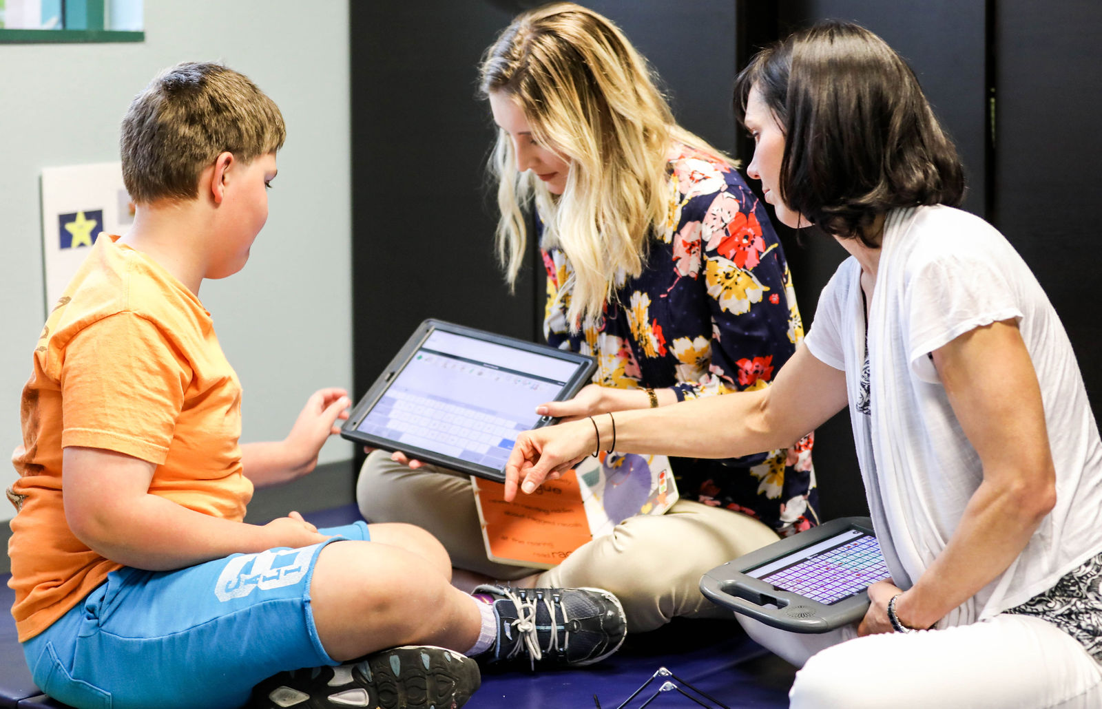 Two speech-language pathologists assisting a young boy using a tablet for communication during a speech therapy session at Speech-N-Motion in San Marcos, California.