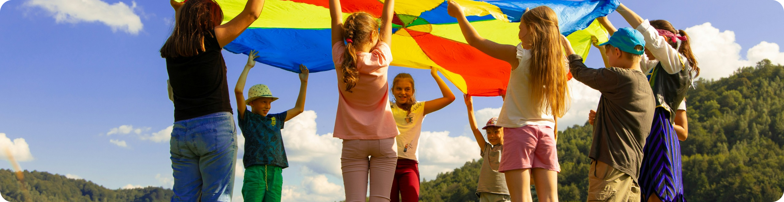 Group of children playing outdoors with a colorful parachute during a speech therapy activity at Speech-N-Motion in North County San Diego.