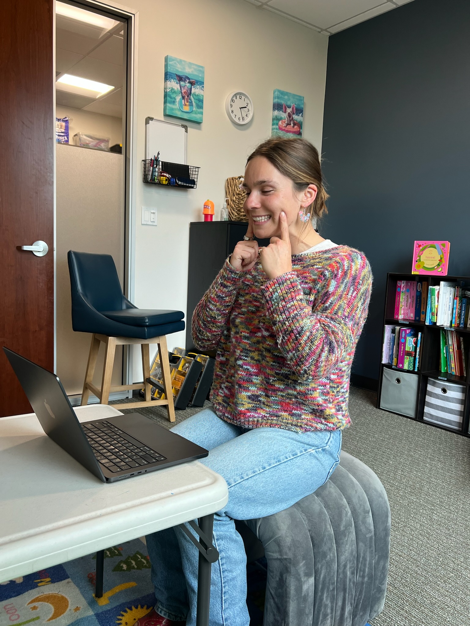 Speech-language pathologist leading a virtual speech therapy session from an office at Speech-N-Motion, demonstrating articulation techniques over video.