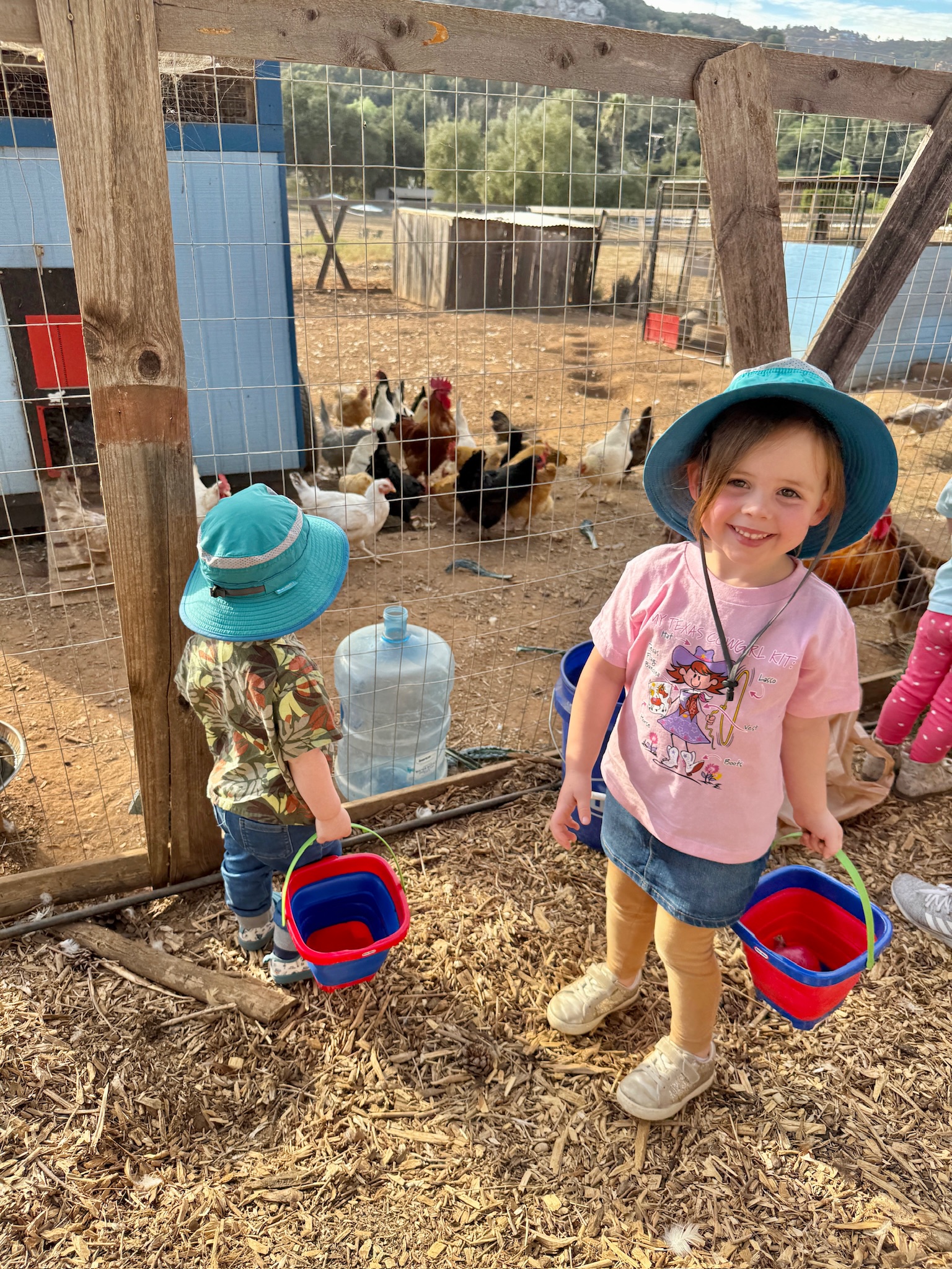 Two children wearing sun hats interacting with animals during a speech therapy session at RoseHaven Farm in Escondido, California.