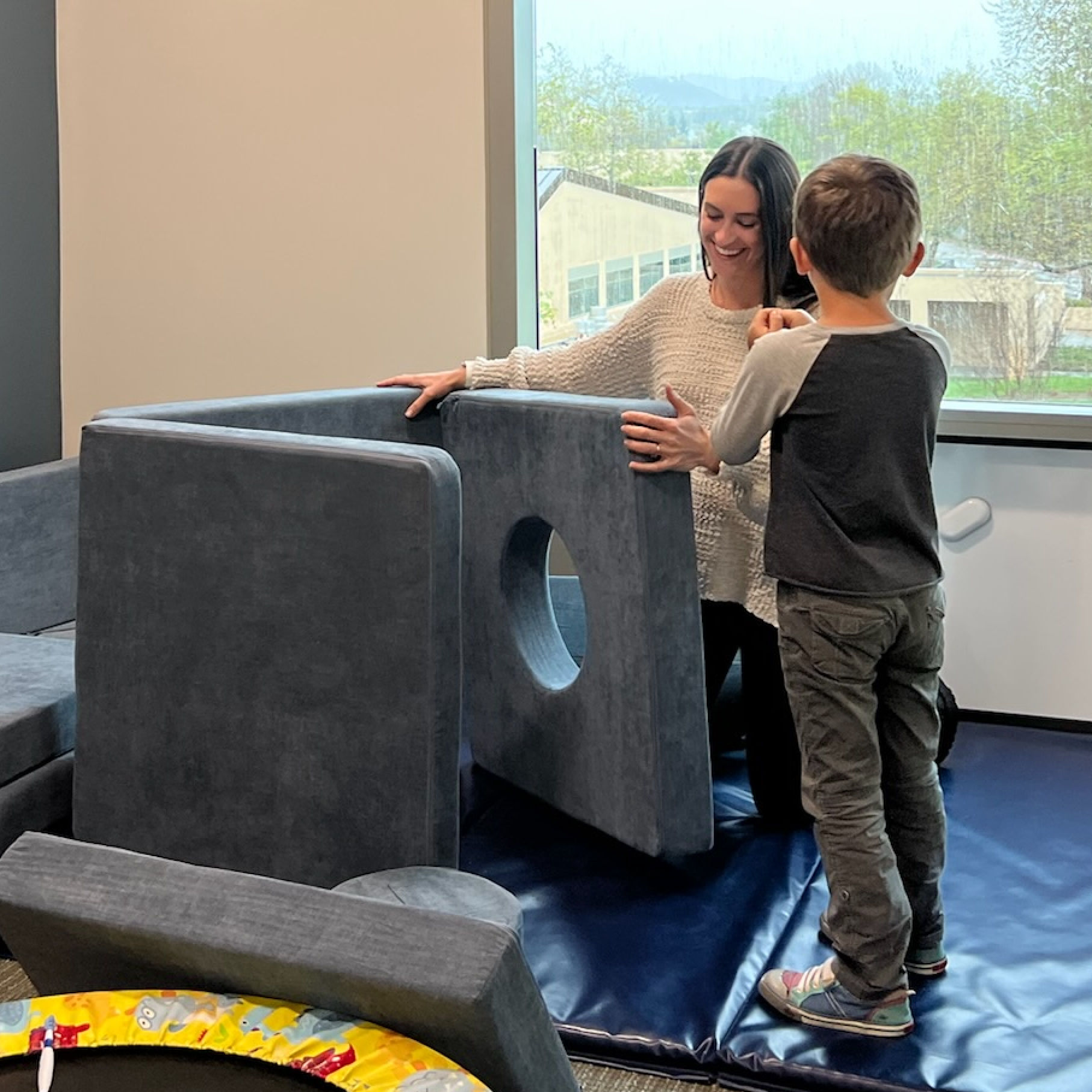 Speech-language pathologist assisting a young child on a padded balance surface during therapy at Speech-N-Motion’s San Marcos clinic.