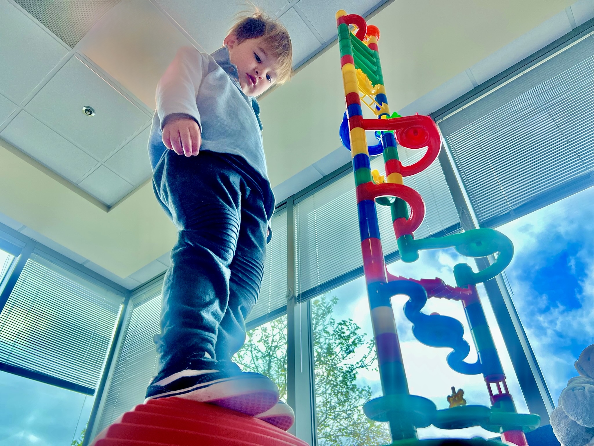 Young boy balancing on a therapy disc beside a tall marble run tower during a speech therapy session at Speech-N-Motion in San Marcos, California.