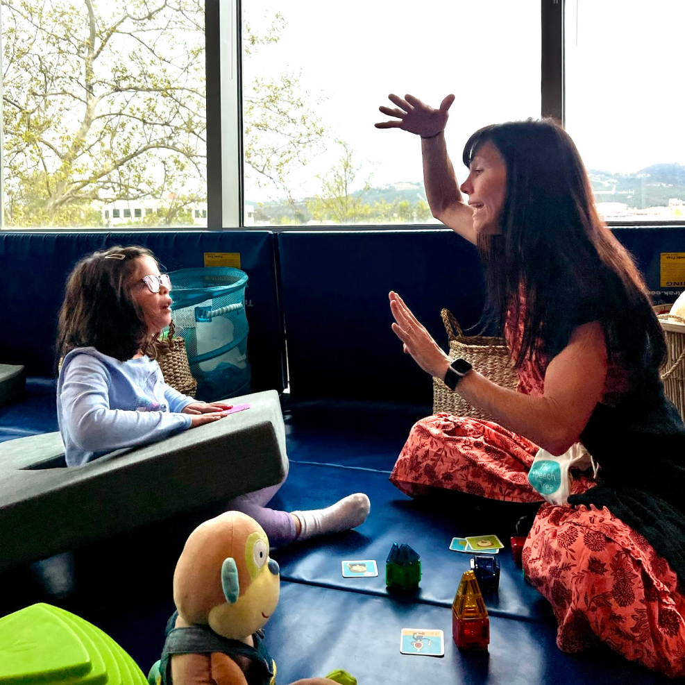 Speech therapist working one-on-one with a young girl on the floor during a speech therapy session at Speech-N-Motion in San Marcos, CA.