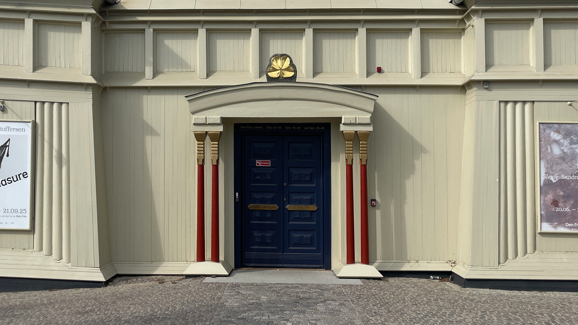 Indgang til den frie udstillingsbygning, med karakteristiske røde søjler på hver side af hoveddøren.