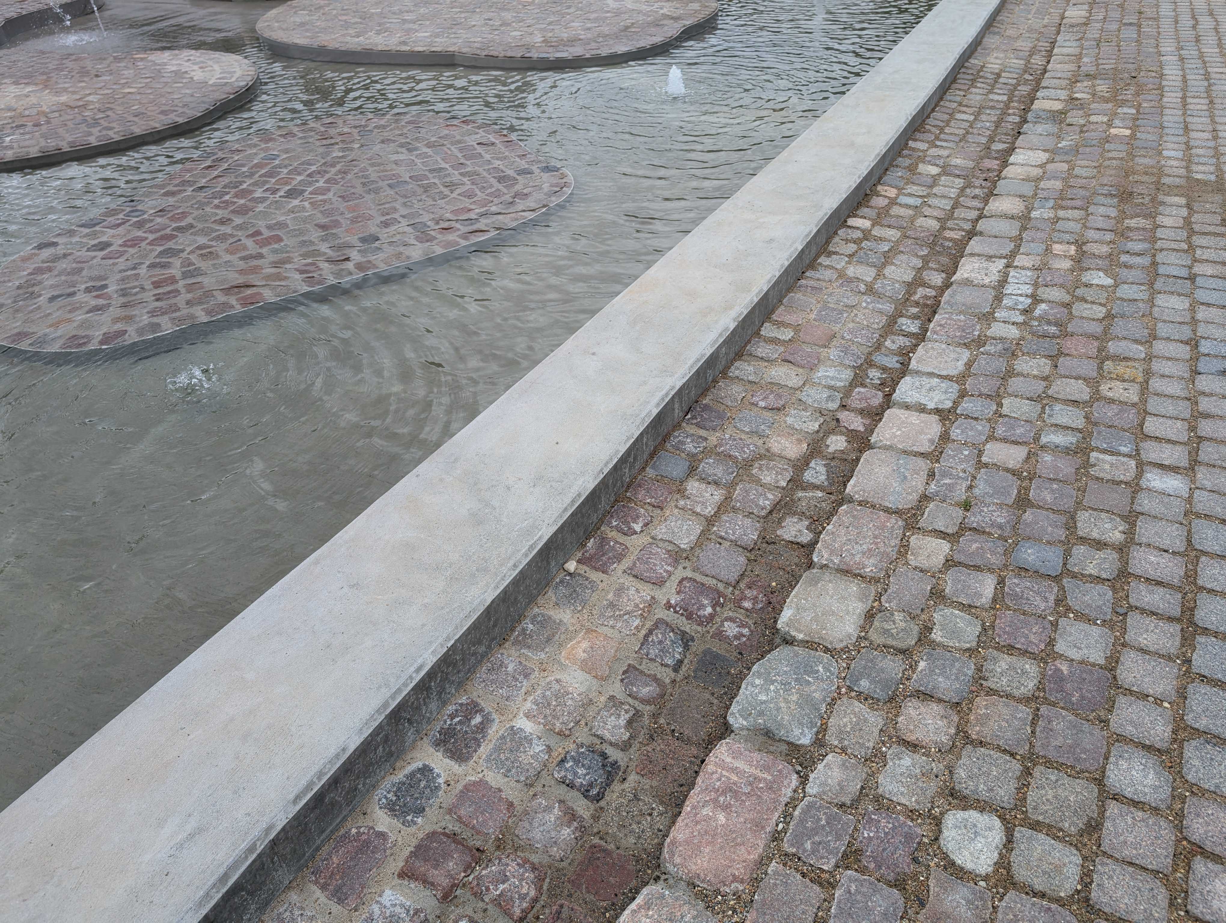 Detaljefoto ved kanten til vandspejlet, med sten i forskellige højder og taktilitet.