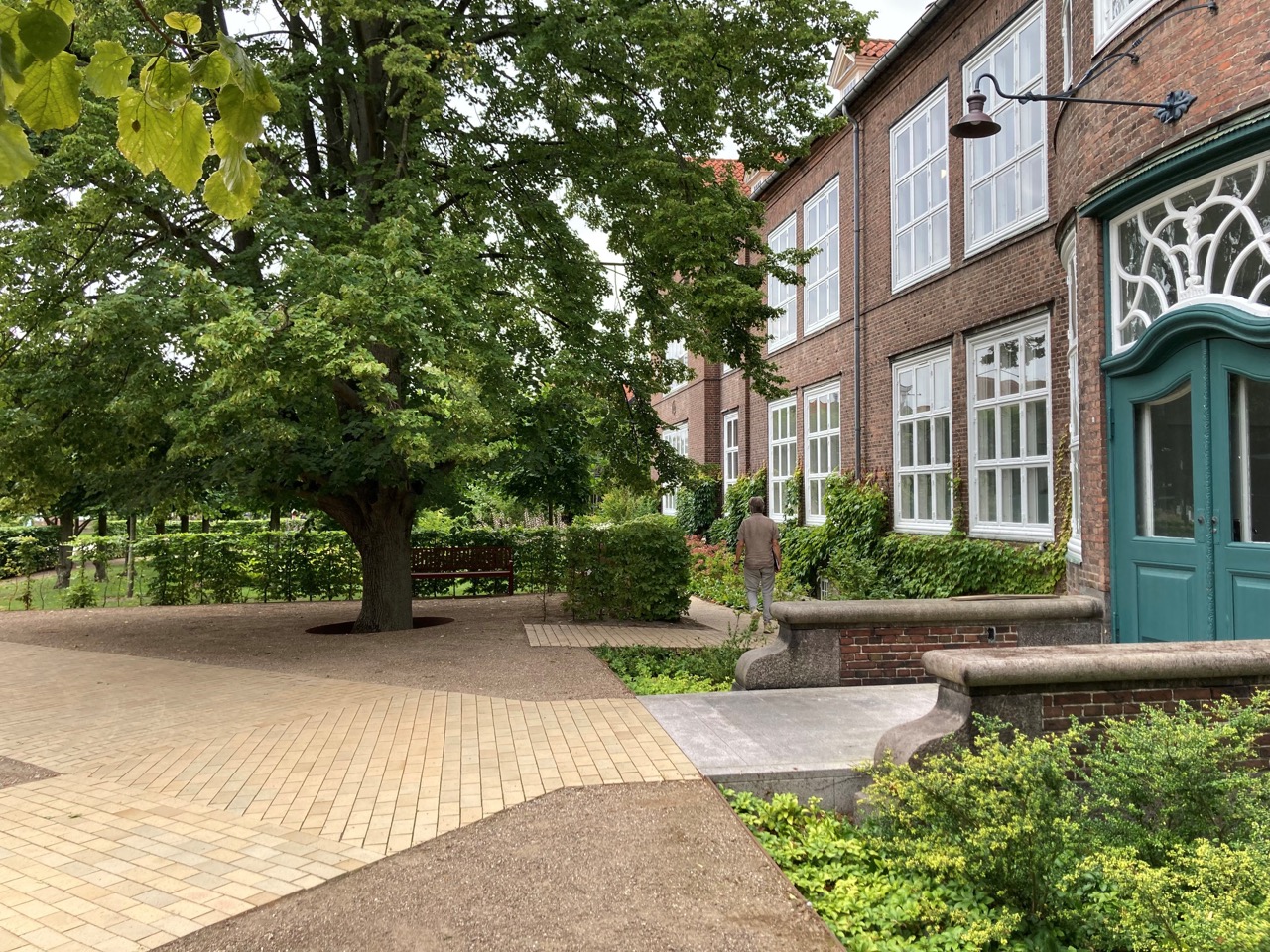 Belægningen fra pladsen foran indgangen til Bispebjerg Hospital, leder brugeren til døren der ligger omringet er smukke grønne planter til hver side af stien.