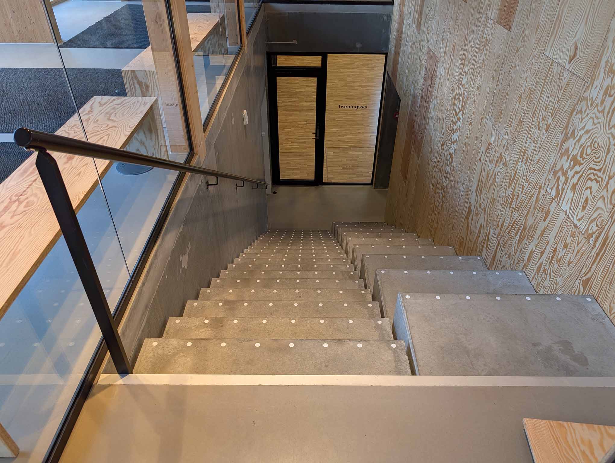 Trappe i beton og træ med håndliste og god bredde, hvor flere personer bevæger sig mellem etager.
