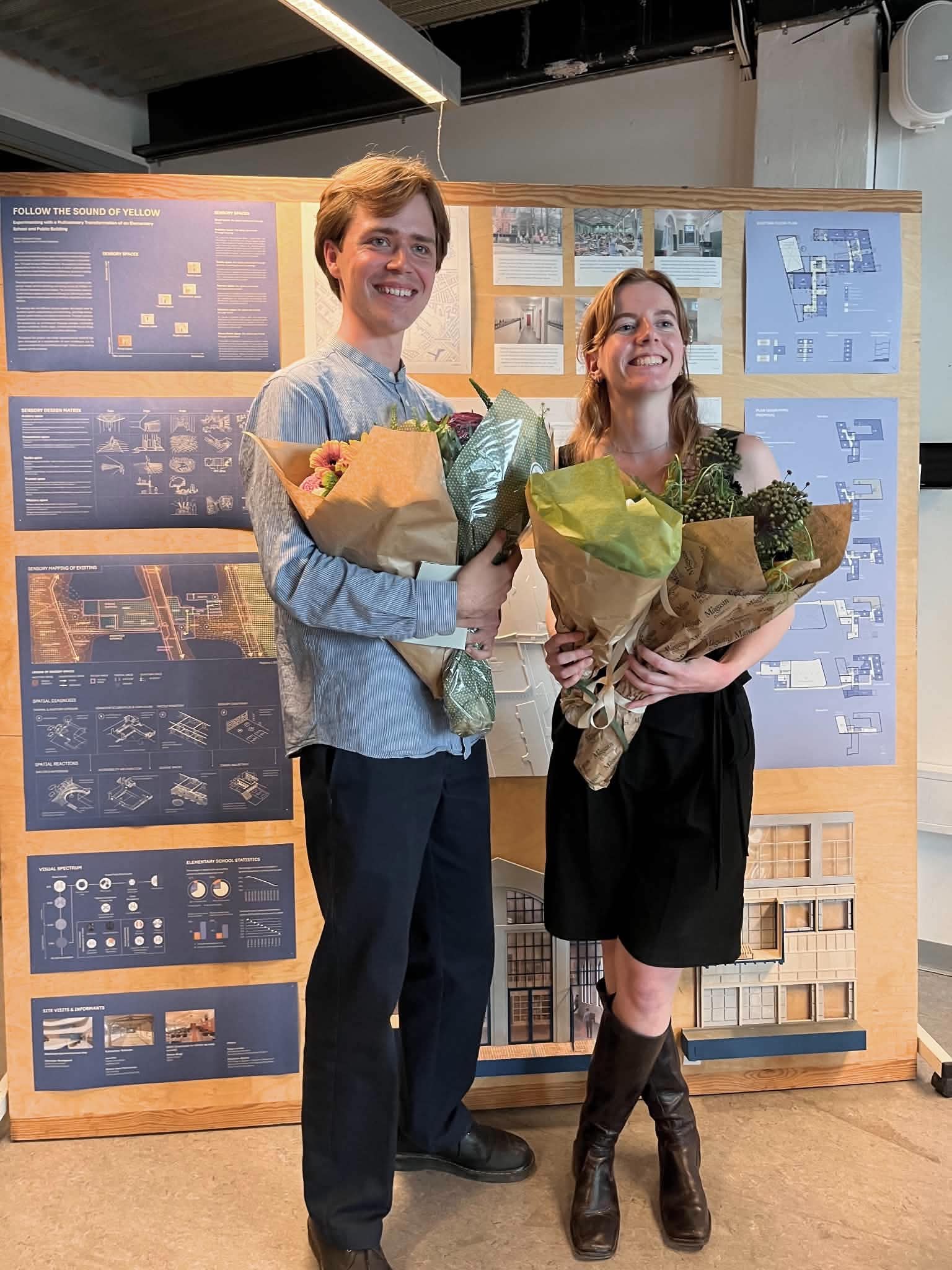Jeppe og Emilie foran plancherne med deres projekt. De holder begge en buket blomster i hånden.
